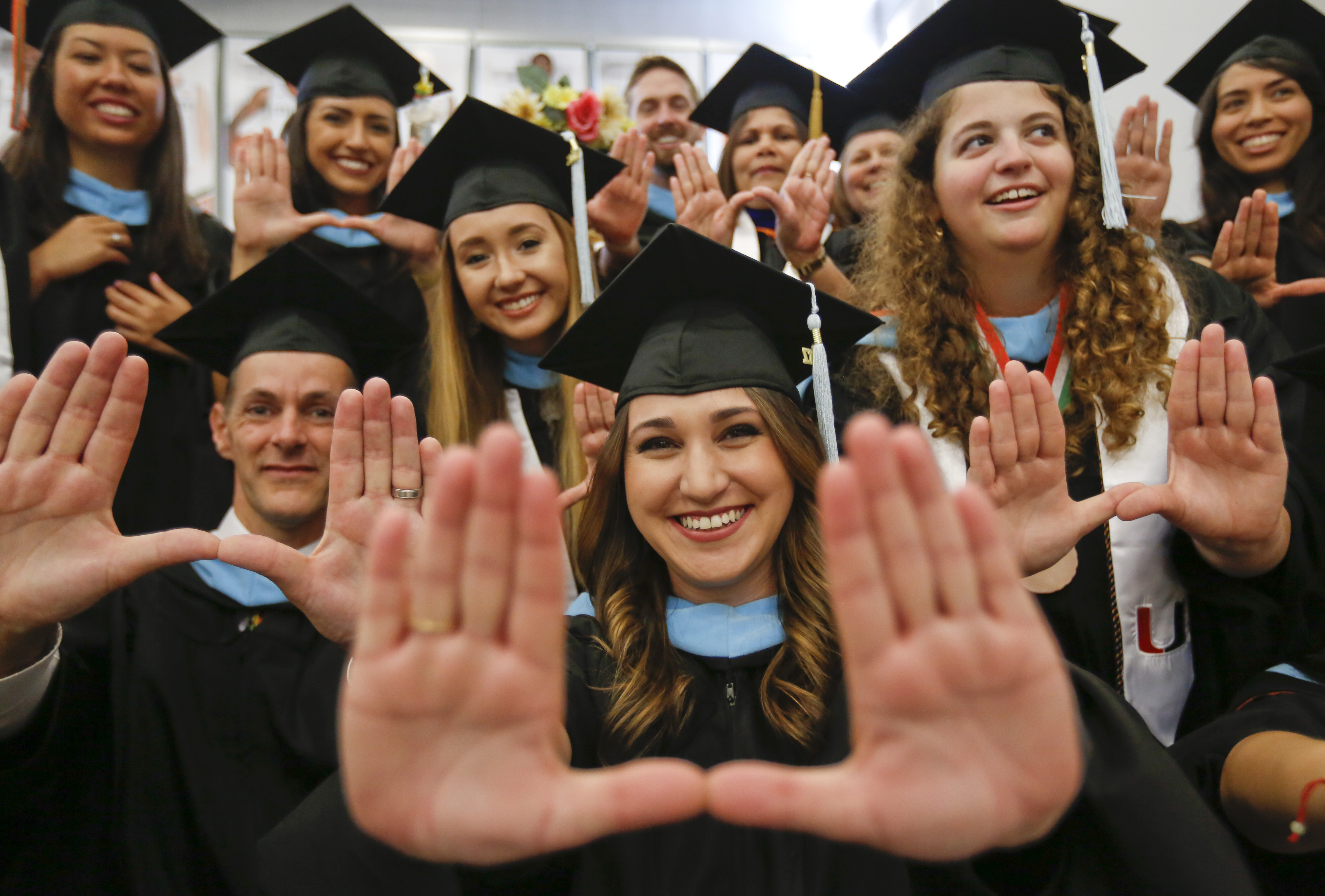 Recent graduates in ceremonial attire and mortarboards hold up the U sign with their hands.