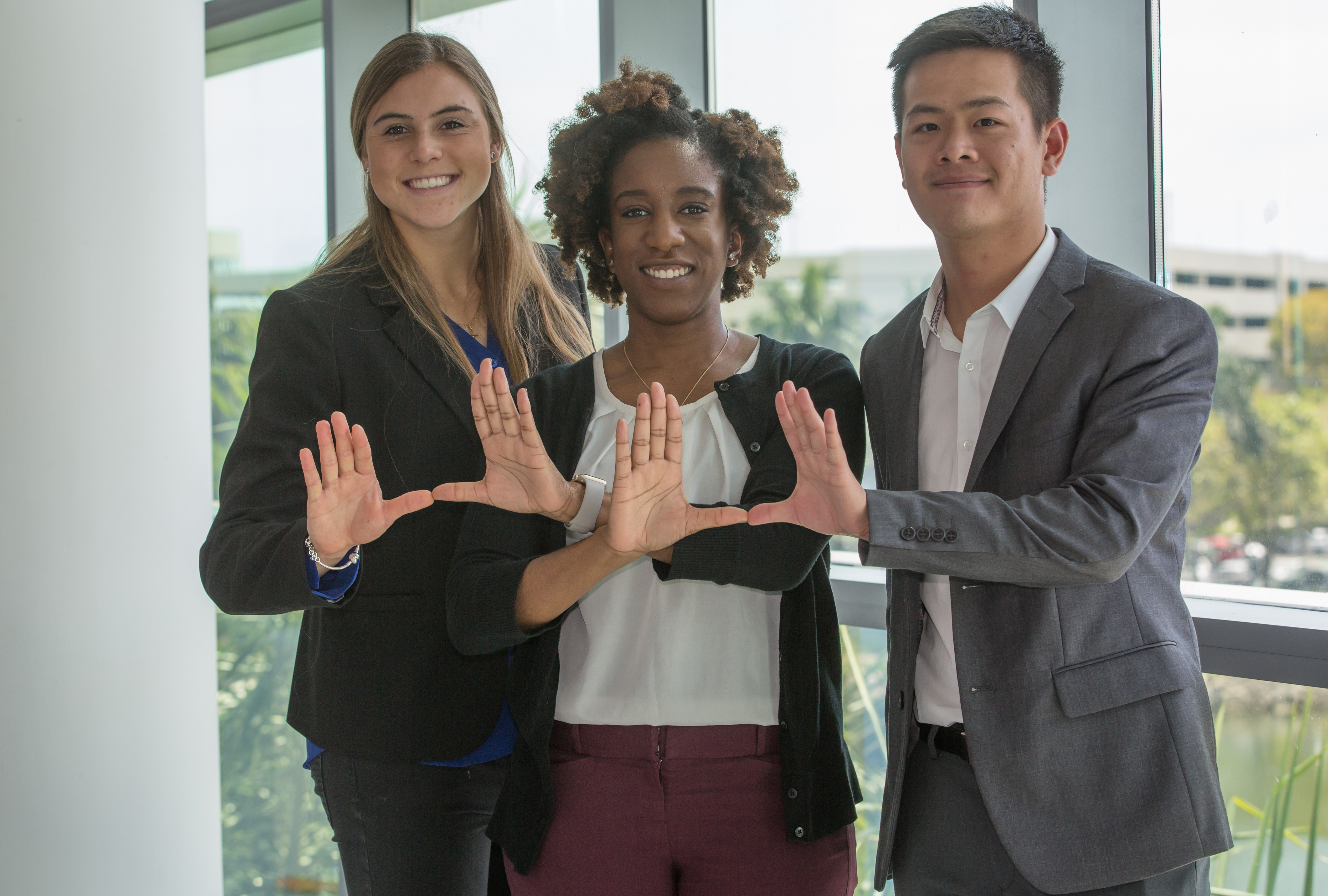 Three graduate students make a U with their hands