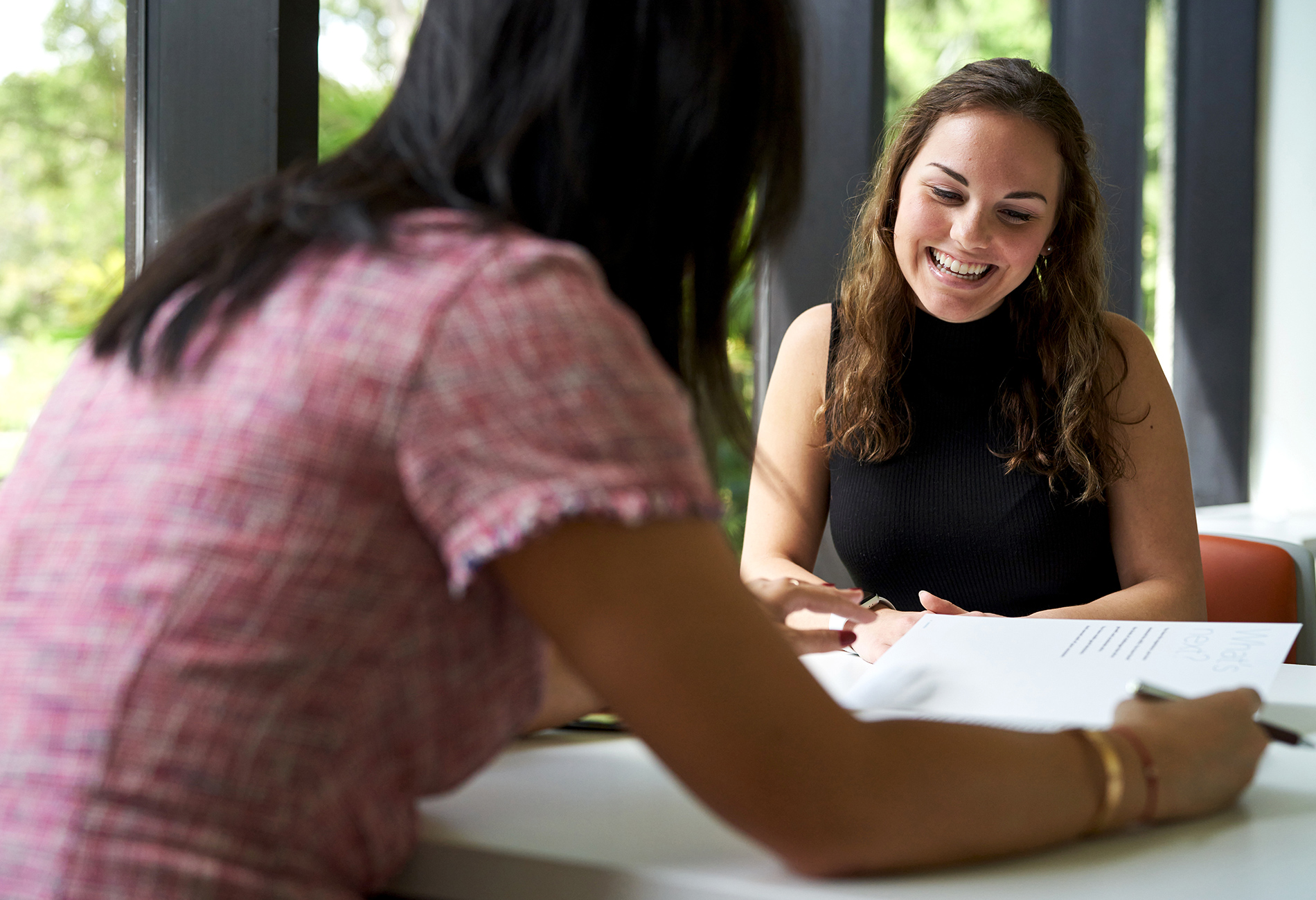 Two female students sit inside discussing programs