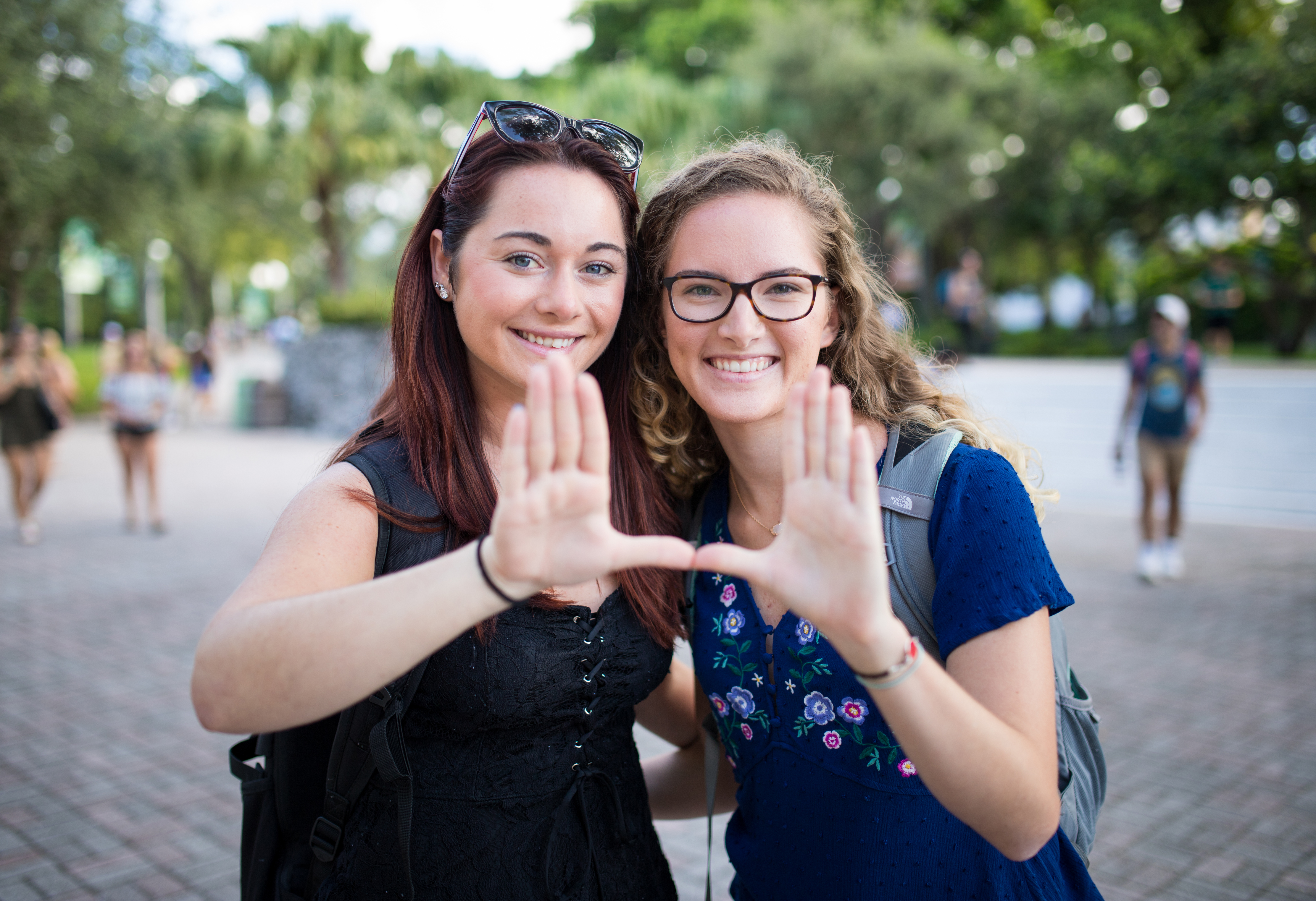 Two students smile and hold their hands together in a "U" shape